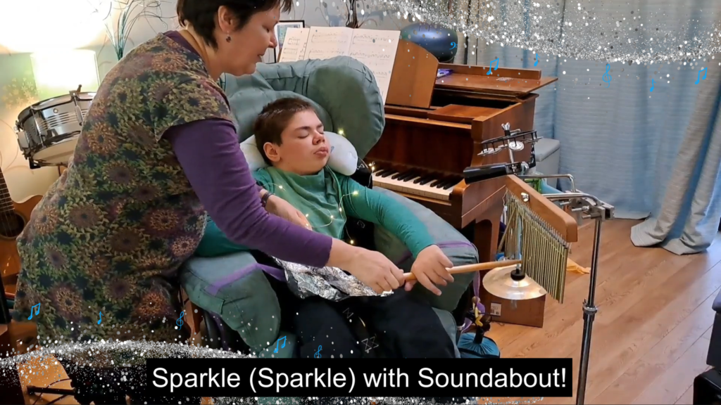 A second screenshot of the video showing a young person playing wind chimes along side a parent/carer